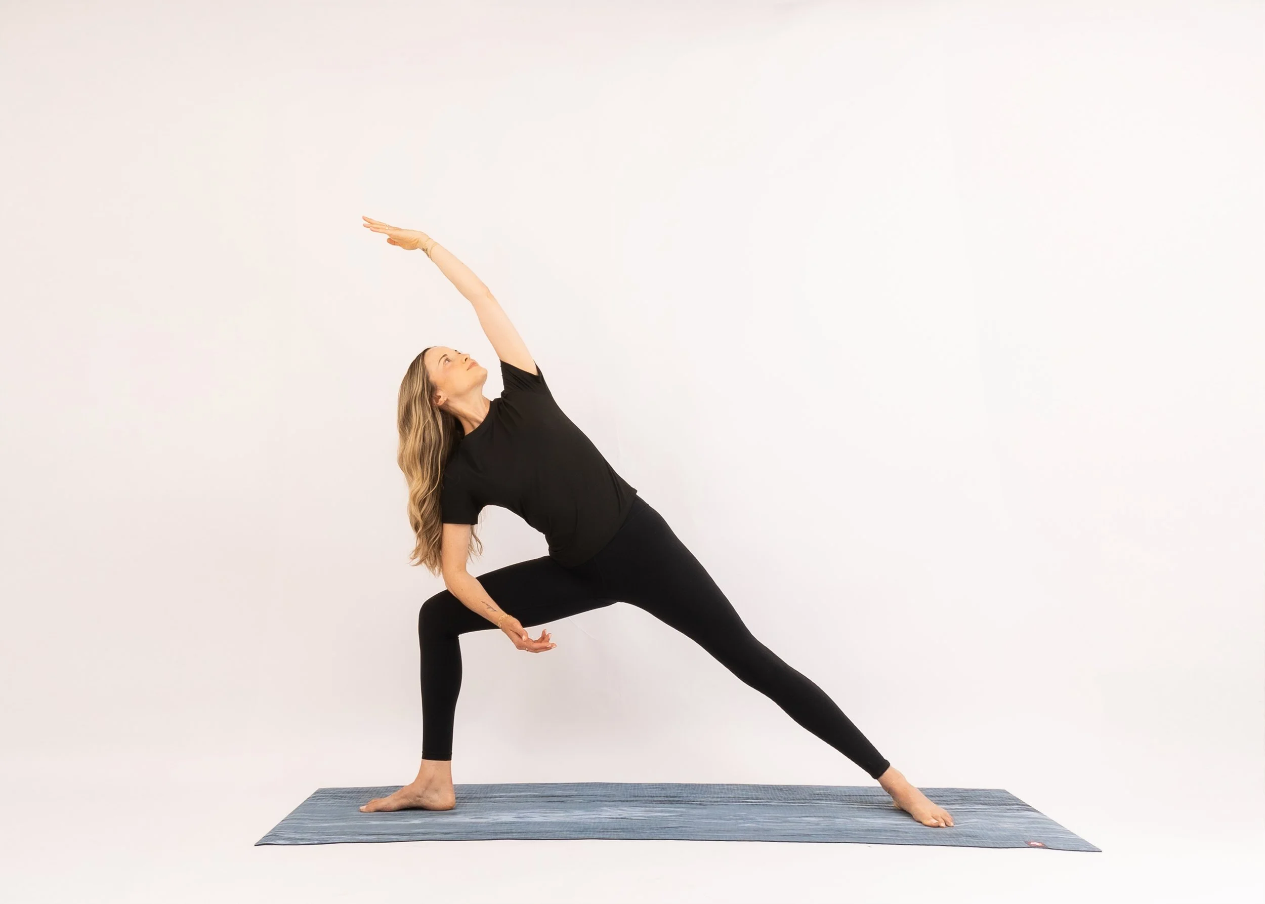 Woman practicing yoga in a challenging side stretch pose on a yoga mat in a studio with a plain white wall.