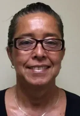 Close-up of a woman smiling, wearing glasses and a dark shirt, with her hair pulled back.
