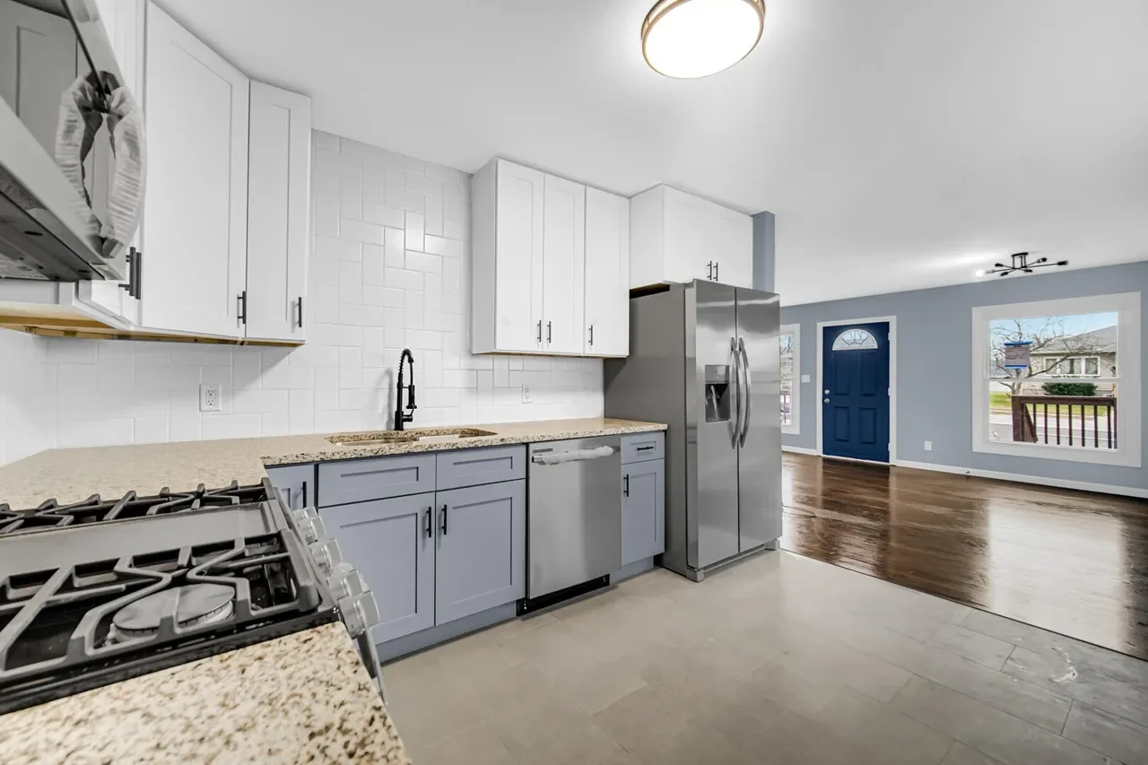 Modern kitchen with white upper cabinets, light blue lower cabinets, granite countertops, stainless steel appliances including a refrigerator and dishwasher, and a white subway tile backsplash.