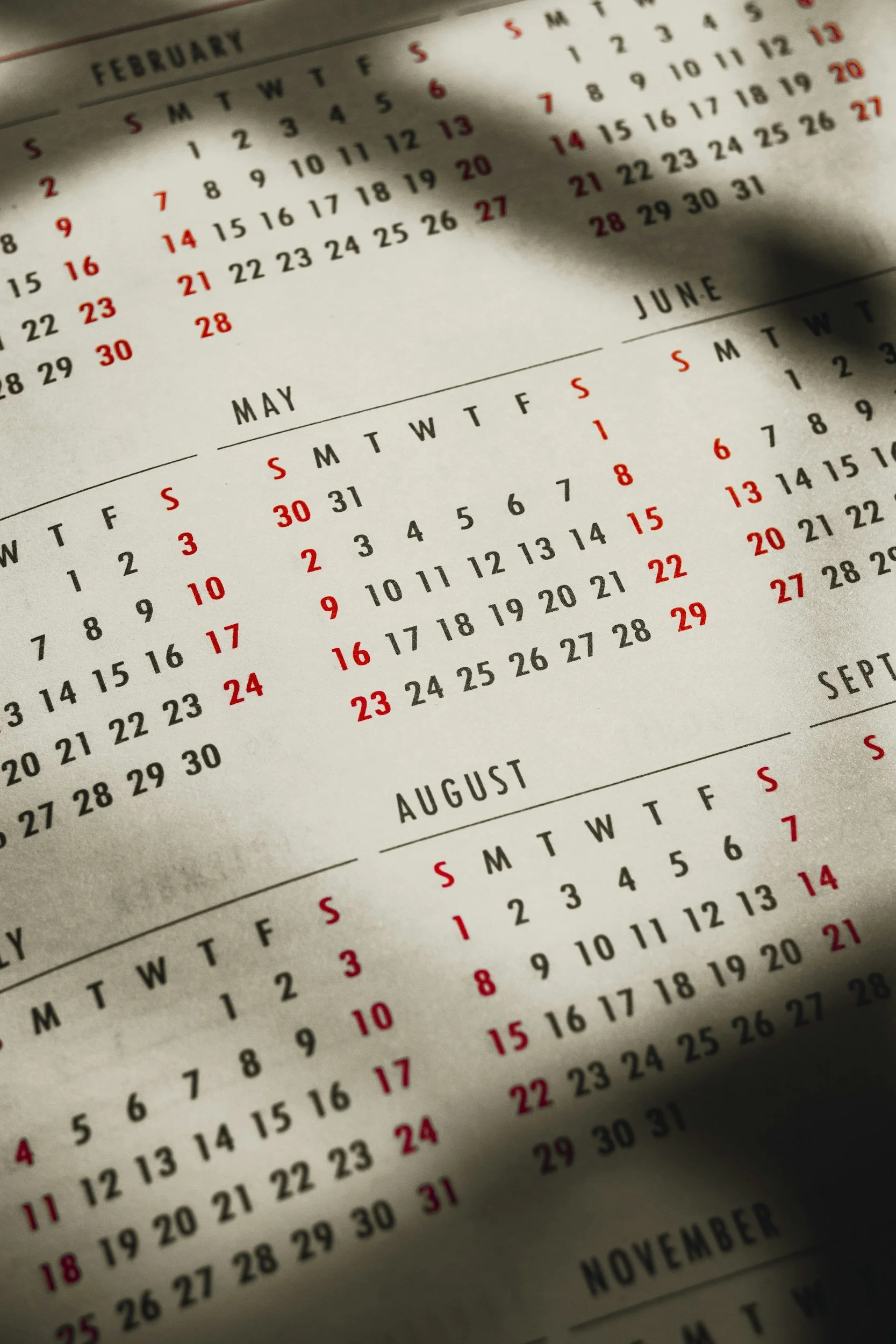 Close-up of a paper calendar showing the months of February, May, June, August, September, October, and November with dates marked in black and weekends in red.