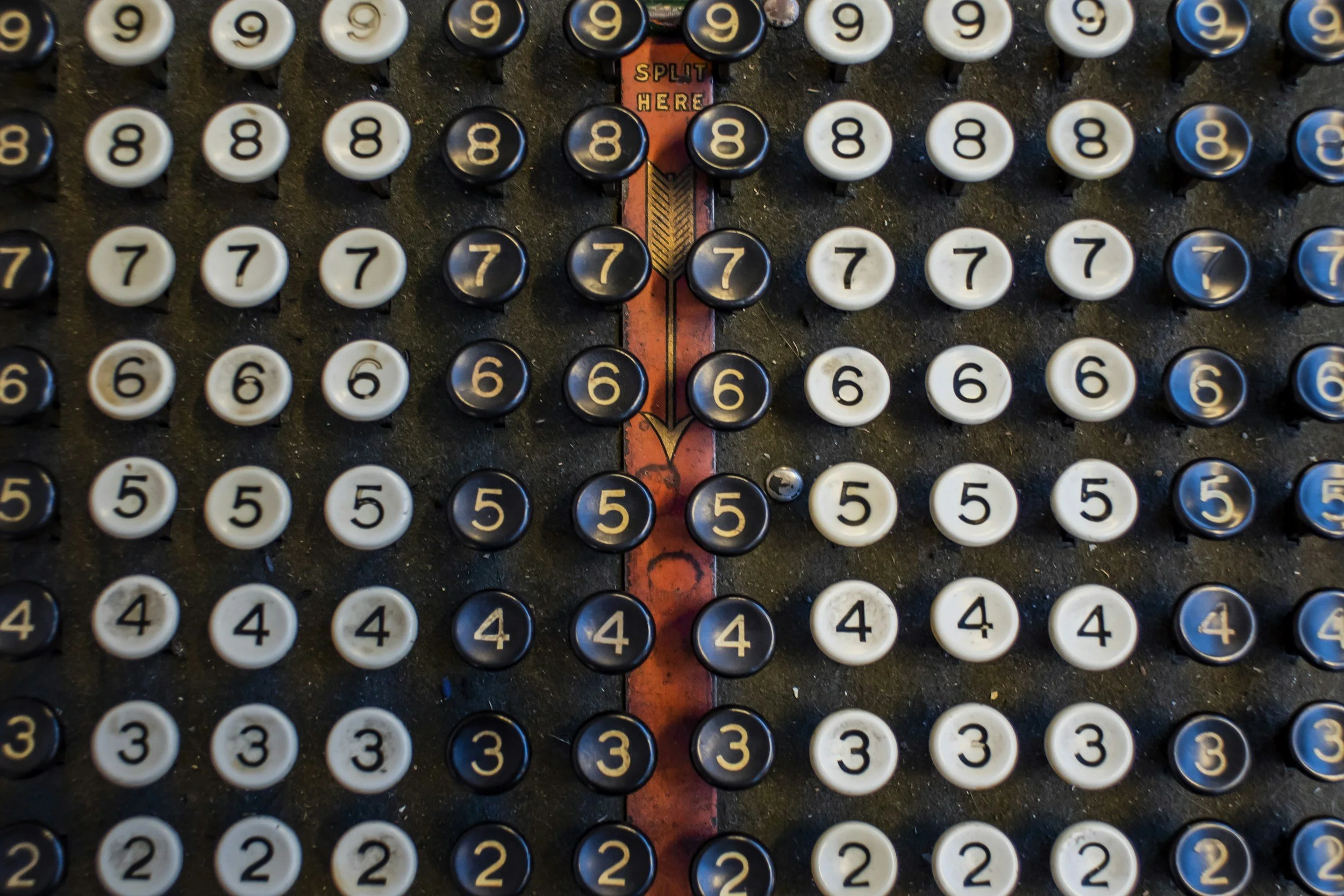 An old vintage typewriter with round keys displaying numbers from 1 to 9, with a red 'Split Here' marker and orange arrow in the center pointing downward.