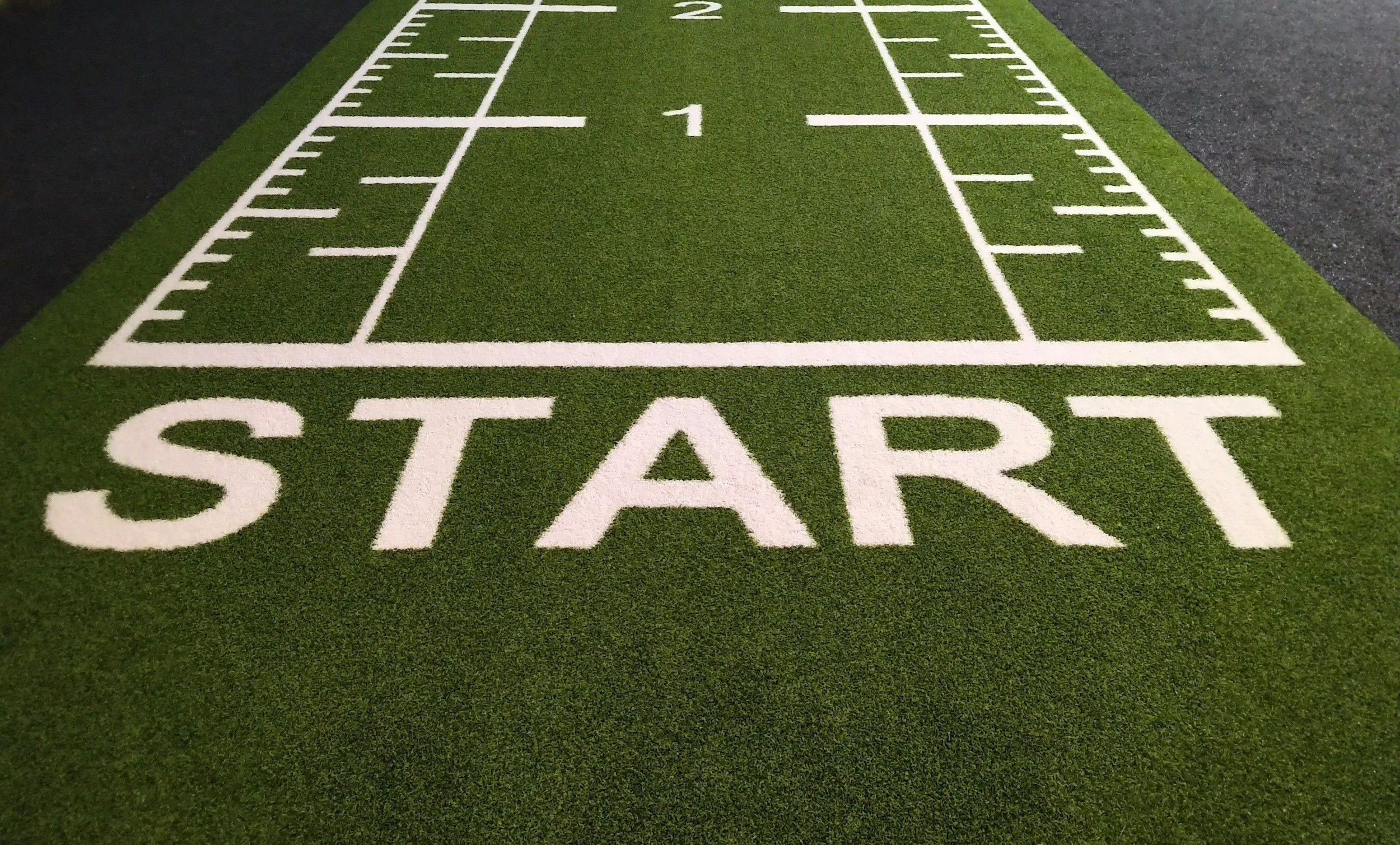 Artificial turf field with white lines marking a sports field and a large white word 'START' at the beginning of the field.