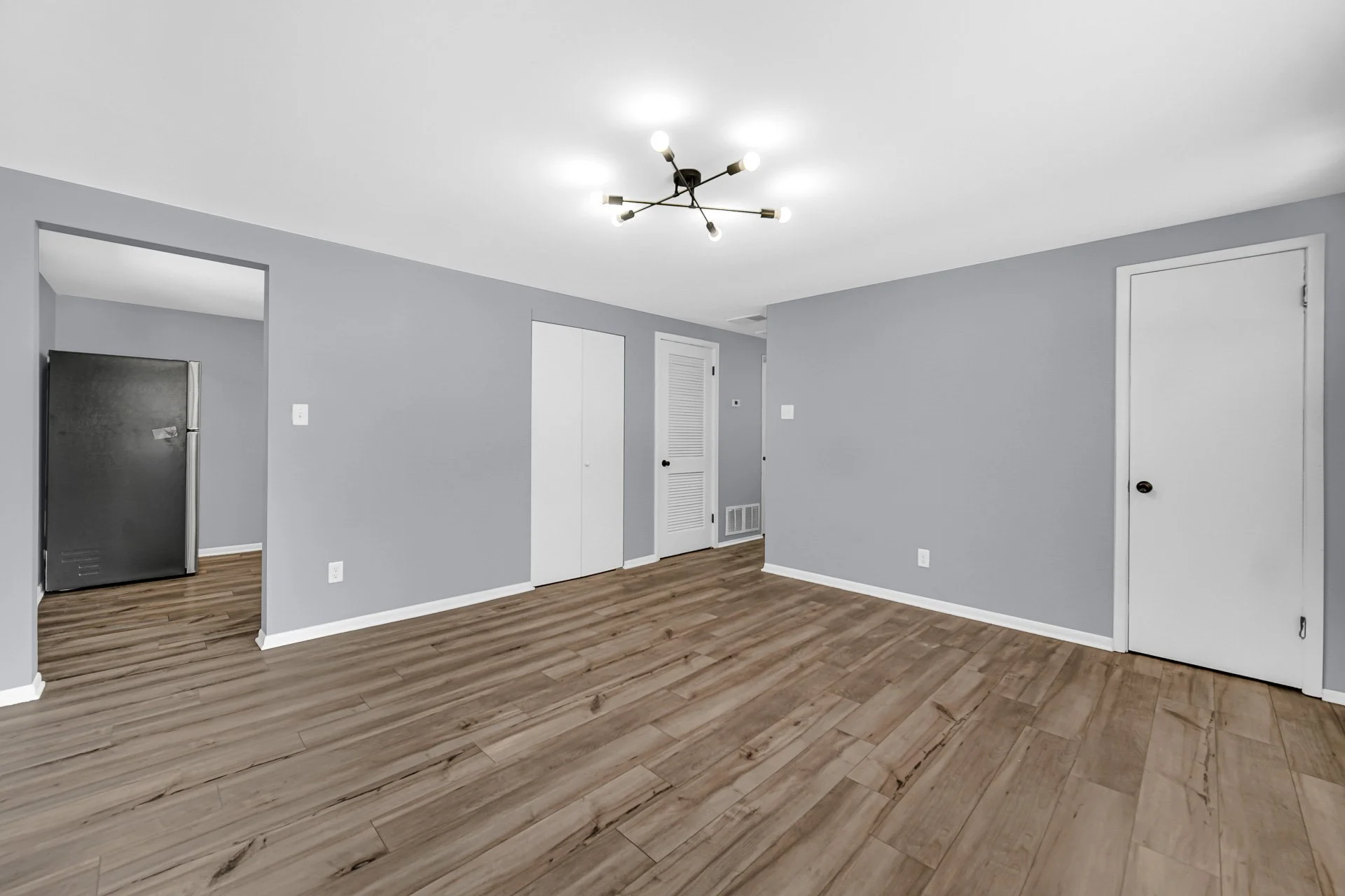 Empty living room with gray walls, wood flooring, and white doors, with a modern black ceiling light fixture.