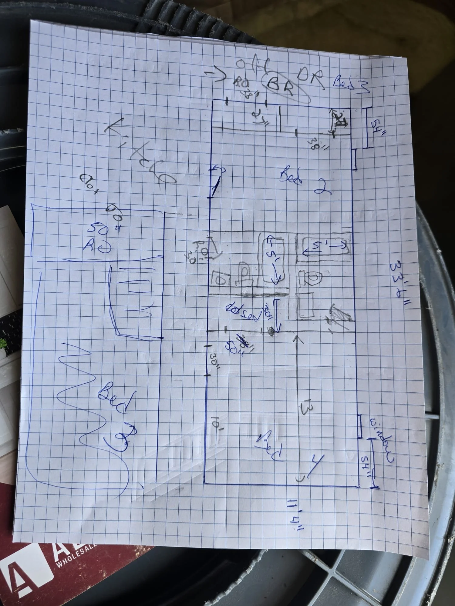 Handwritten floor plan diagram on graph paper showing dimensions and layout for a home interior, including bedrooms, bathroom, living room, and kitchen.