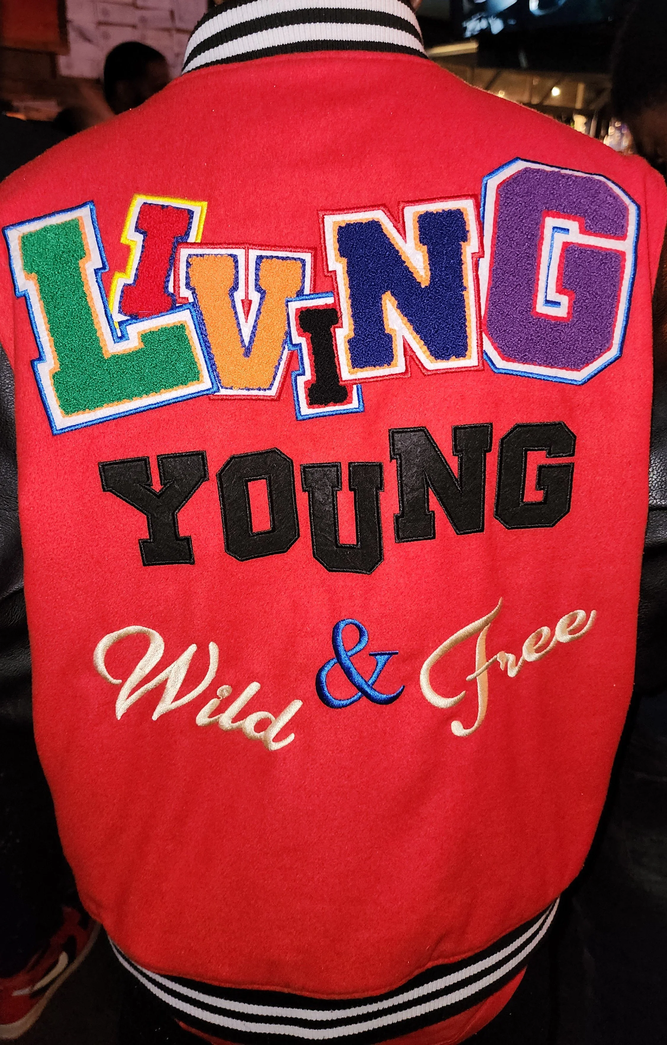 Back of a person wearing a red jacket with colorful embroidered letters spelling 'LIVING' and the words 'Wild & Free' below.