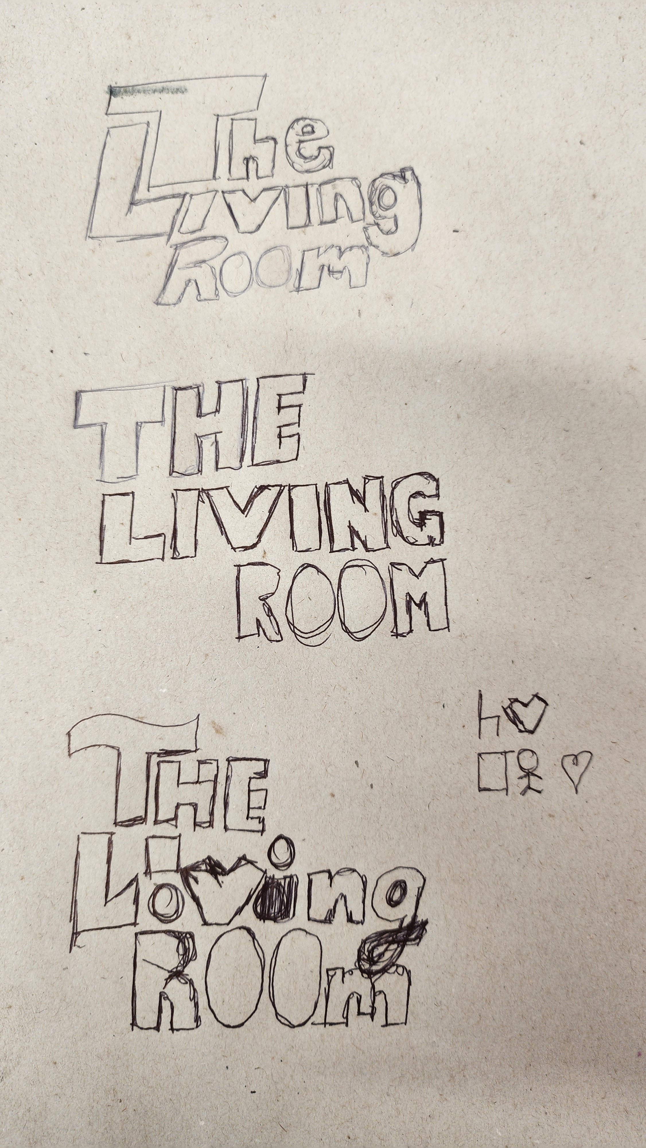 Hand-drawn message on paper saying "The Living Room," with small doodles of hearts and stick figures.