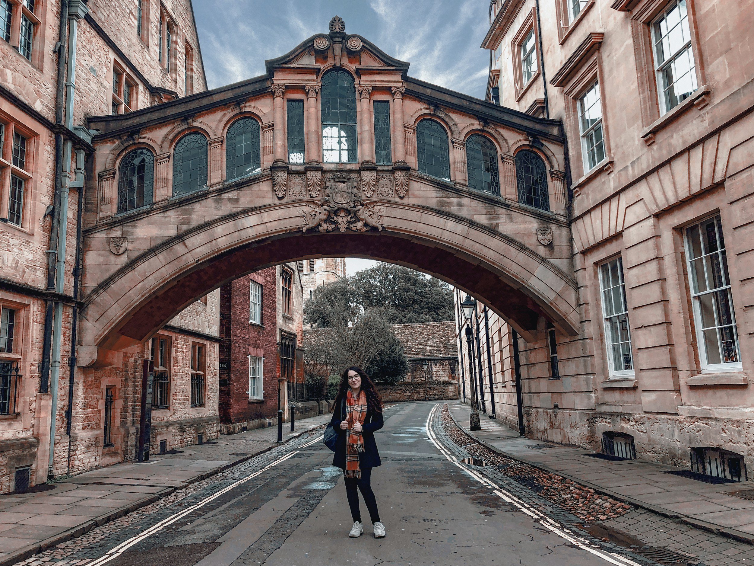 Woman standing under historic stone archway in a narrow street with old brick buildings on either side.