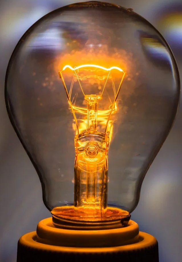 Close-up of an incandescent light bulb turned on, glowing with a warm orange light.