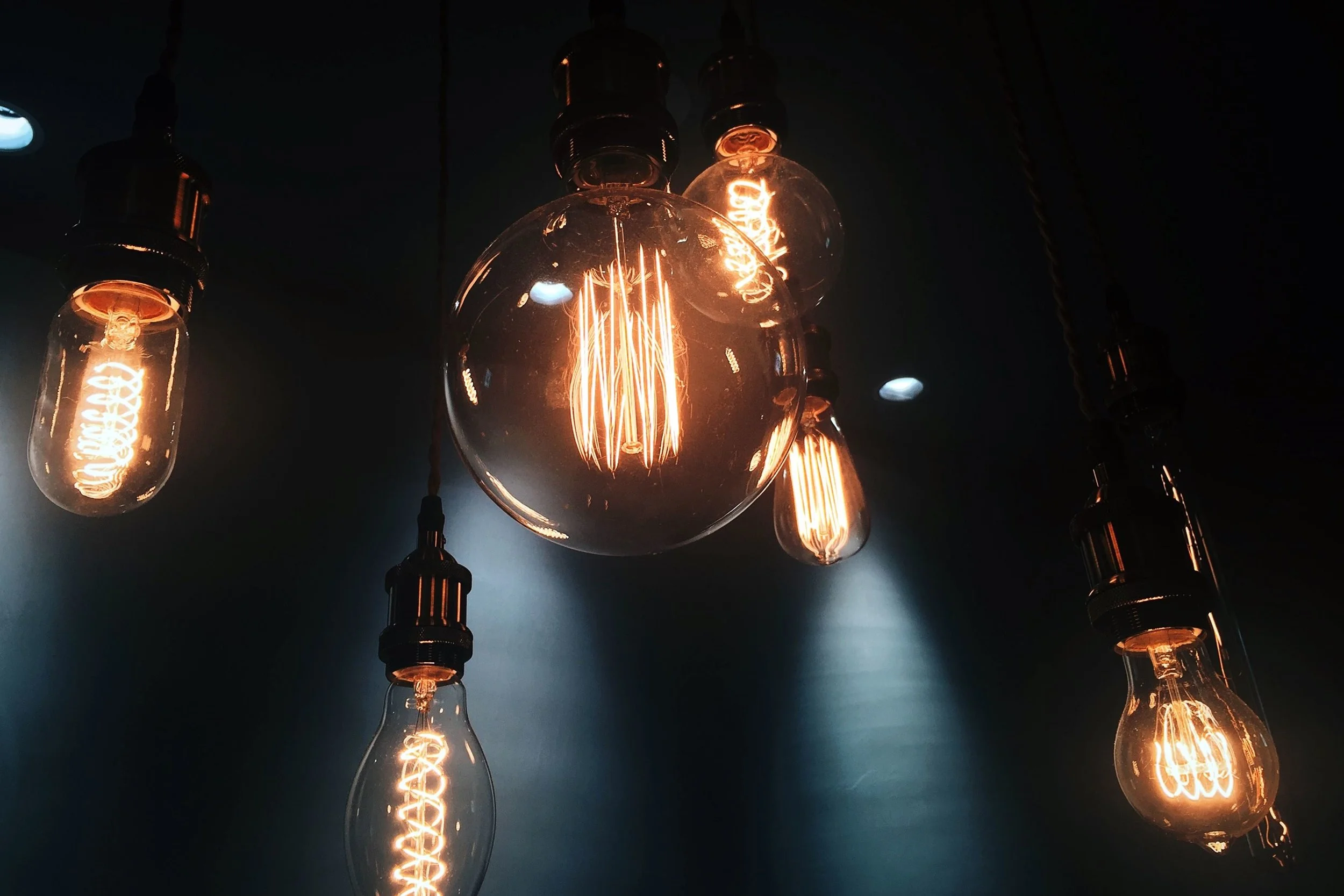 Multiple vintage-style Edison light bulbs hanging from cords on a dark ceiling, glowing warmly with visible filaments.