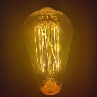 Close-up of an illuminated vintage incandescent light bulb with glowing filament against a dark background.