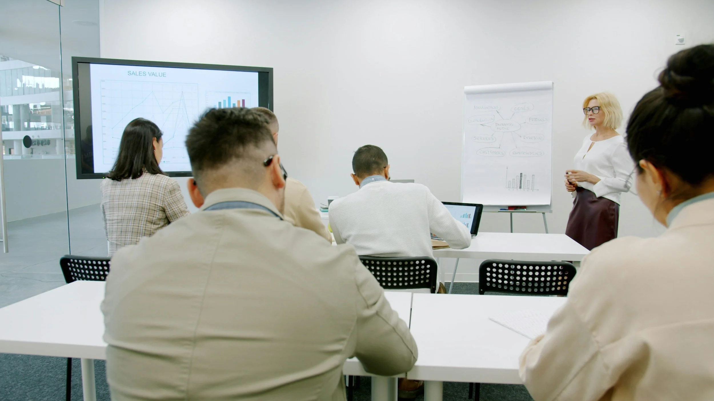 Business meeting in a modern conference room with a presenter and audience, a large screen displaying graphs and a whiteboard with diagrams.