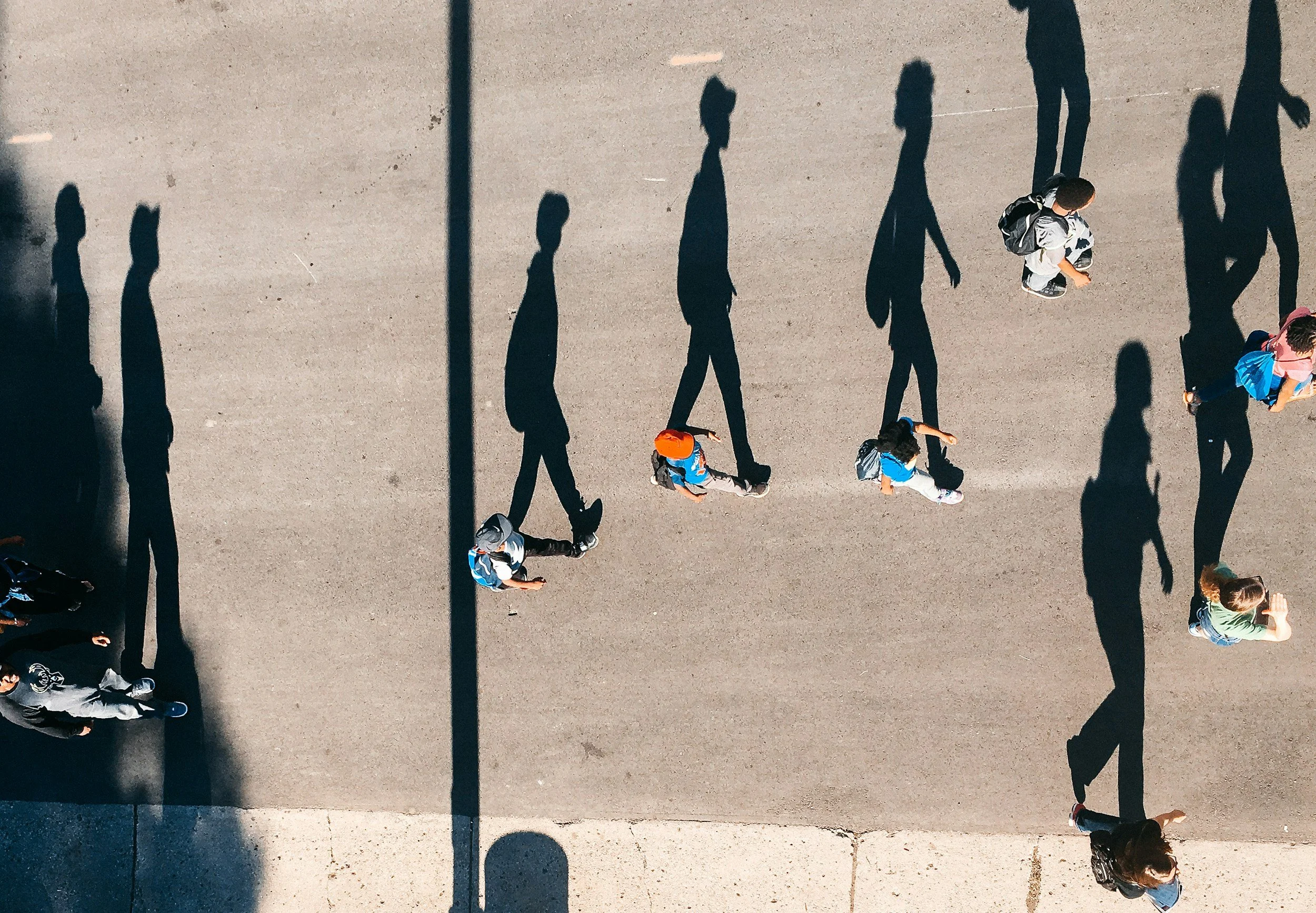 People walking on a sidewalk, their shadows cast on the ground during daylight.