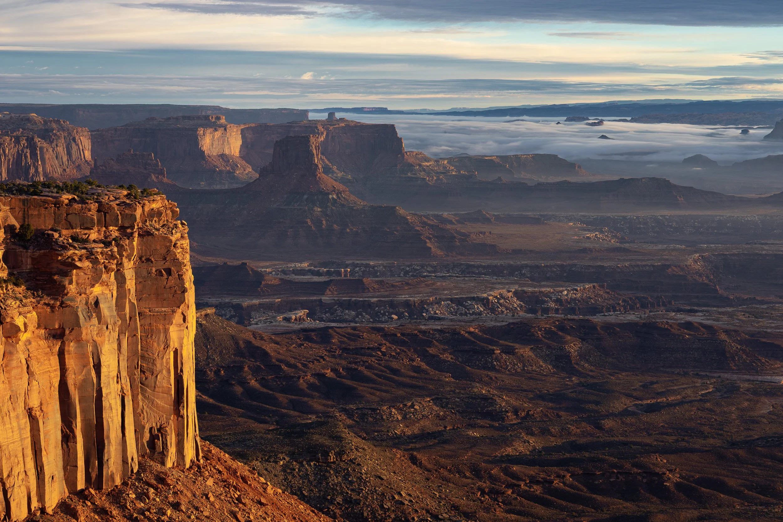 A scenic view of the Grand Canyon during sunrise or sunset, with layered rock formations, canyon walls, and a sky filled with clouds and light.