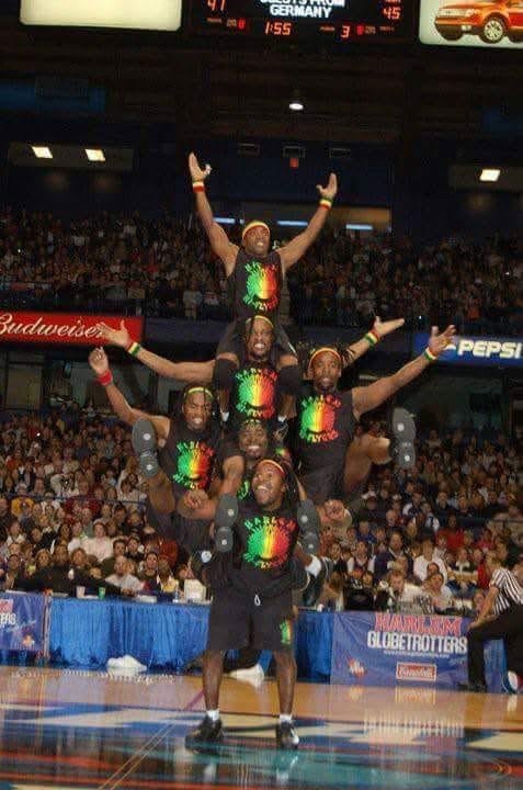 A team of six performers in matching outfits forming a human pyramid during a performance in an indoor arena with a crowd watching.