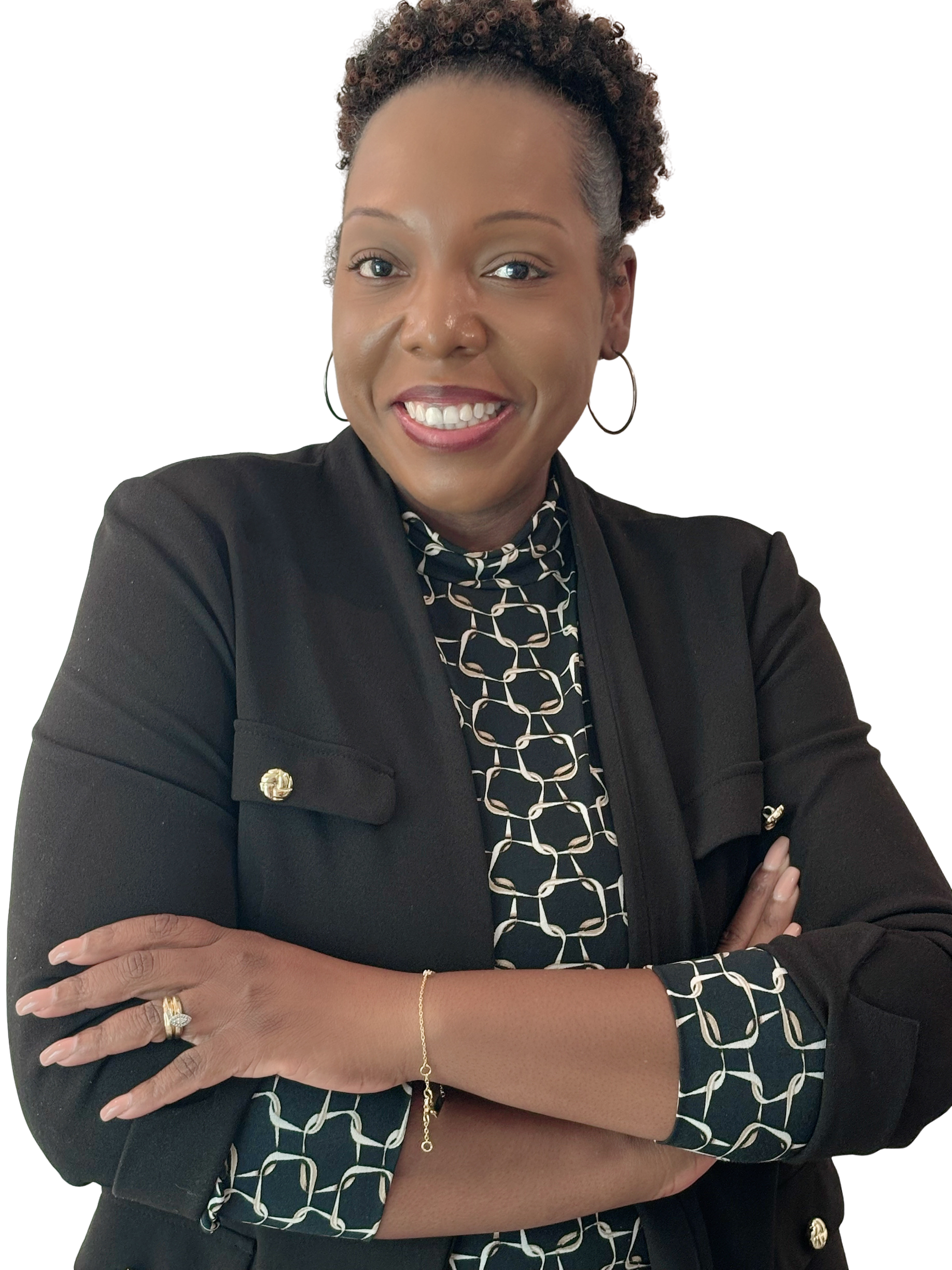 A smiling woman with short curly hair wearing a black blazer with gold buttons, a patterned blouse, hoop earrings, and a gold bracelet, posing with crossed arms in front of a plain white background.