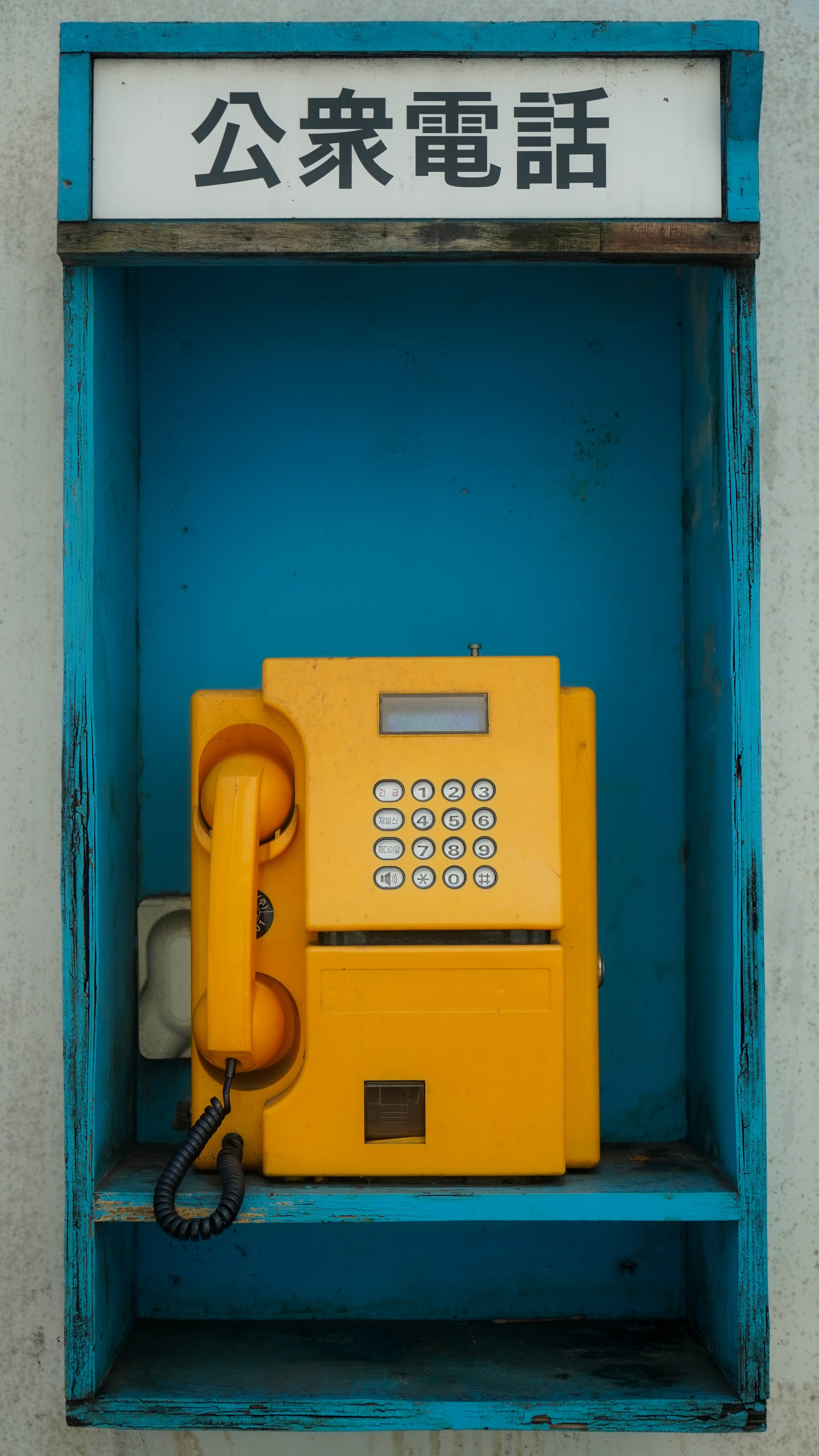 Une cabine téléphonique bleue contenant un téléphone public jaune.