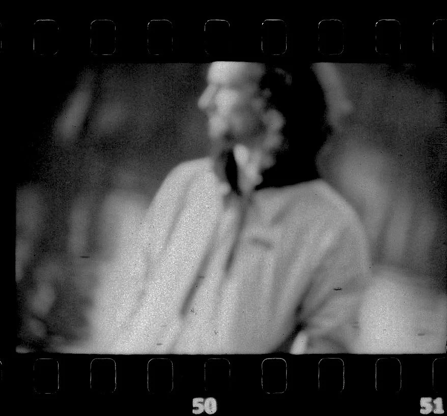 Une photo en noir et blanc floue d'une personne portant une veste, avec une silhouette indistincte en arrière-plan.