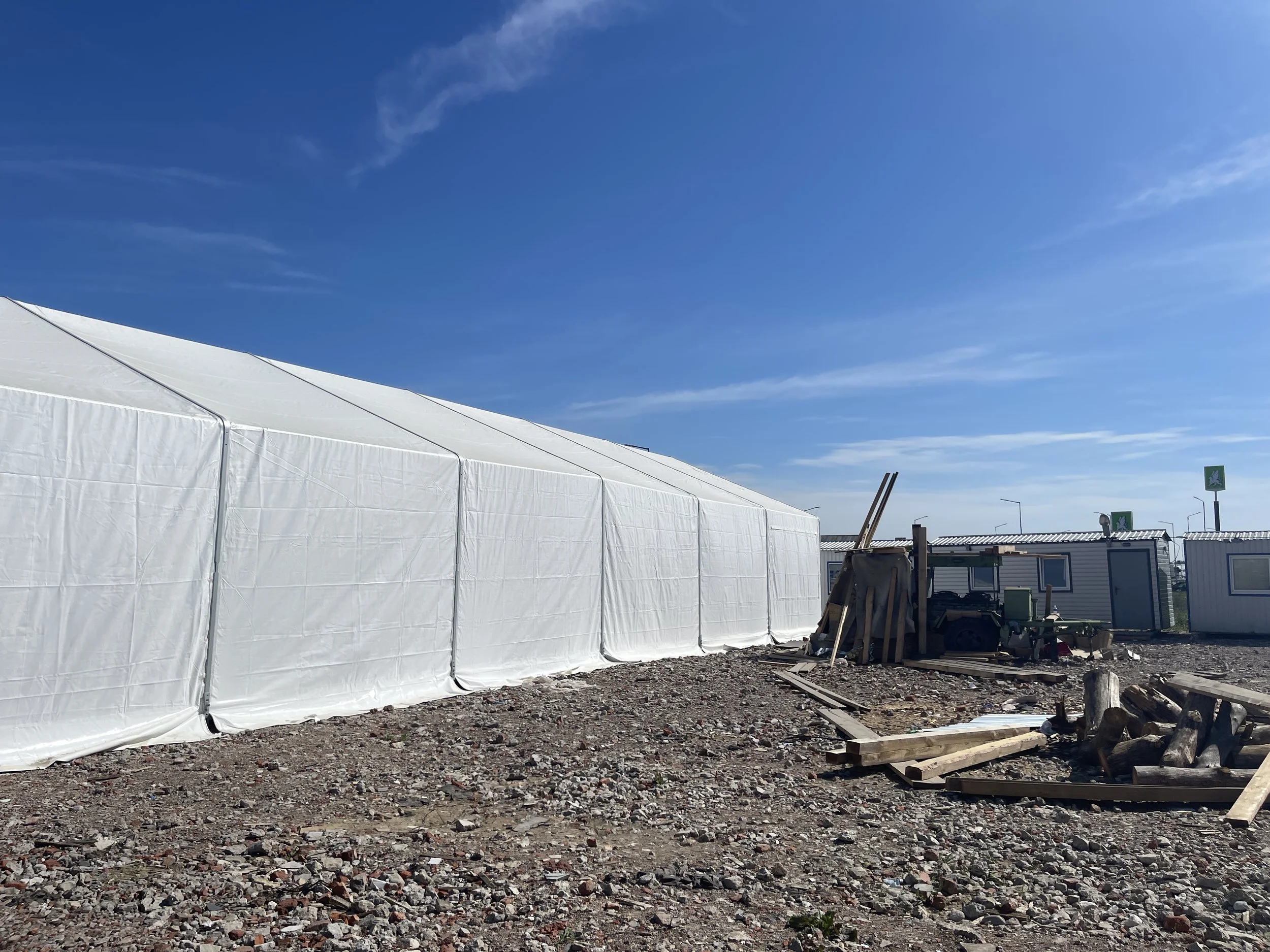 Large white tent set up outdoors on a rocky ground under a clear blue sky.