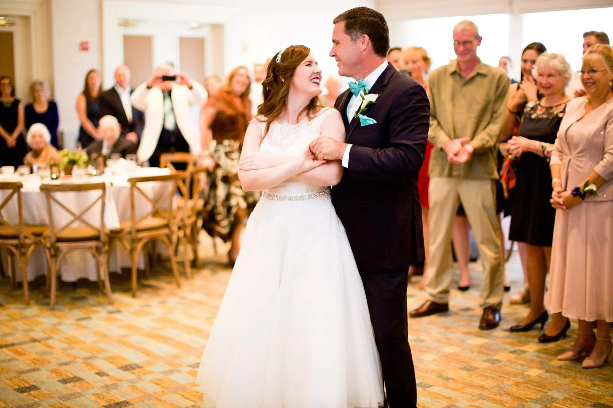Bride and groom sharing a dance at their wedding reception, surrounded by happy guests.