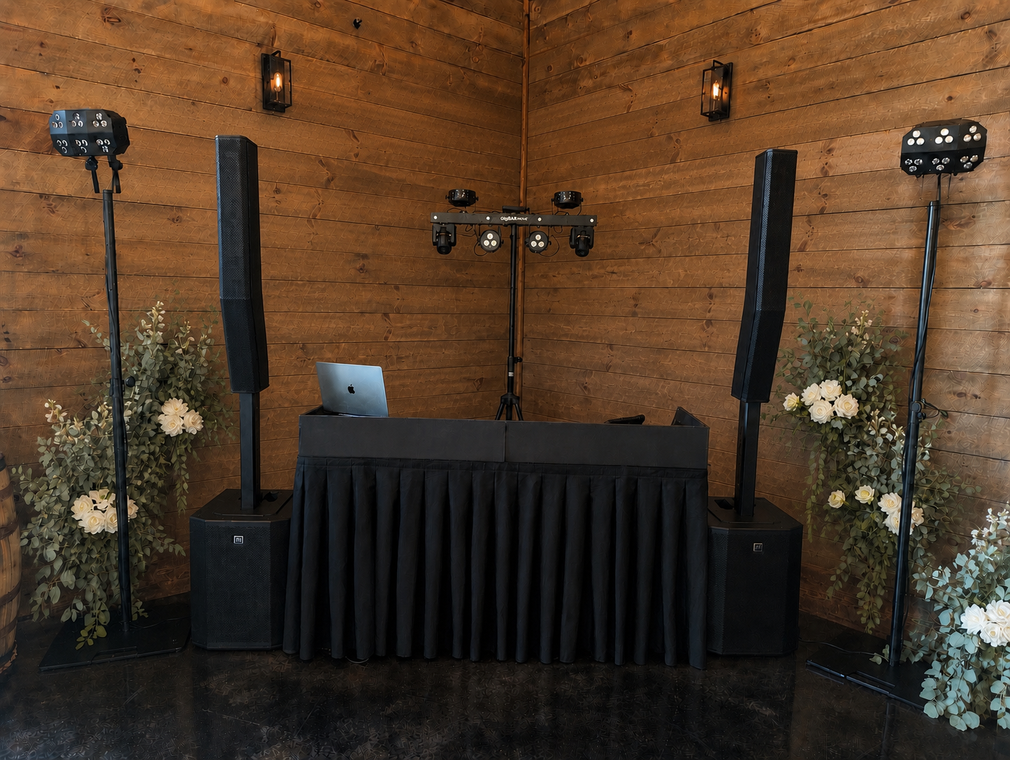 DJ setup with large speakers, lighting equipment, and floral arrangements in a wooden-paneled room.