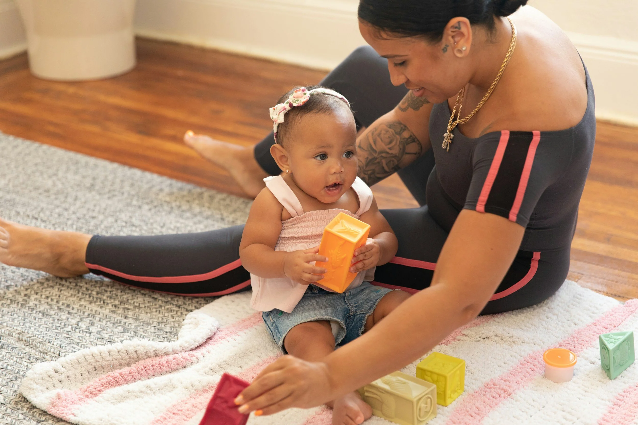A woman and a young girl sitting on a rug and playing with colorful blocks.
