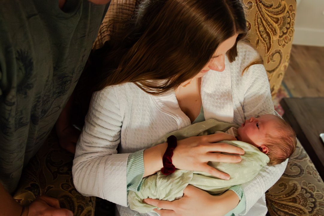 A woman holding a newborn baby in her arms, looking down lovingly at the baby.
