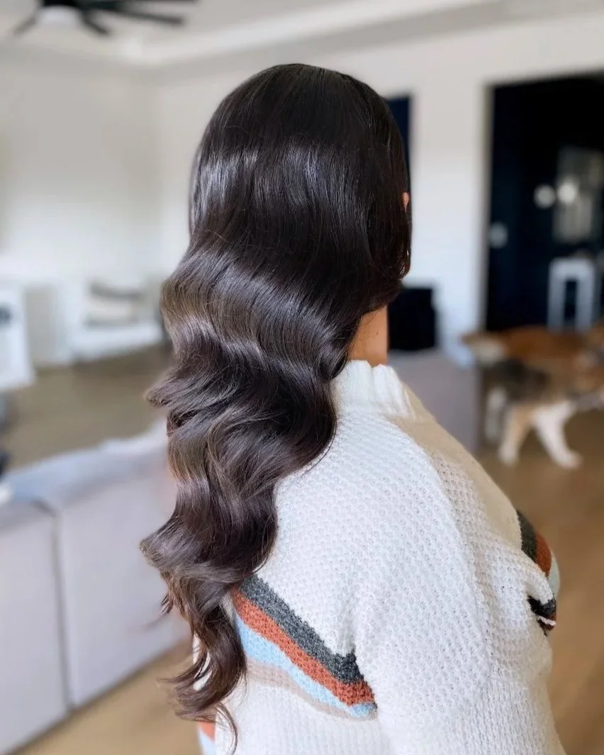 Side view of a woman with glossy, wavy dark hair, wearing a white sweater with colorful stripes.
