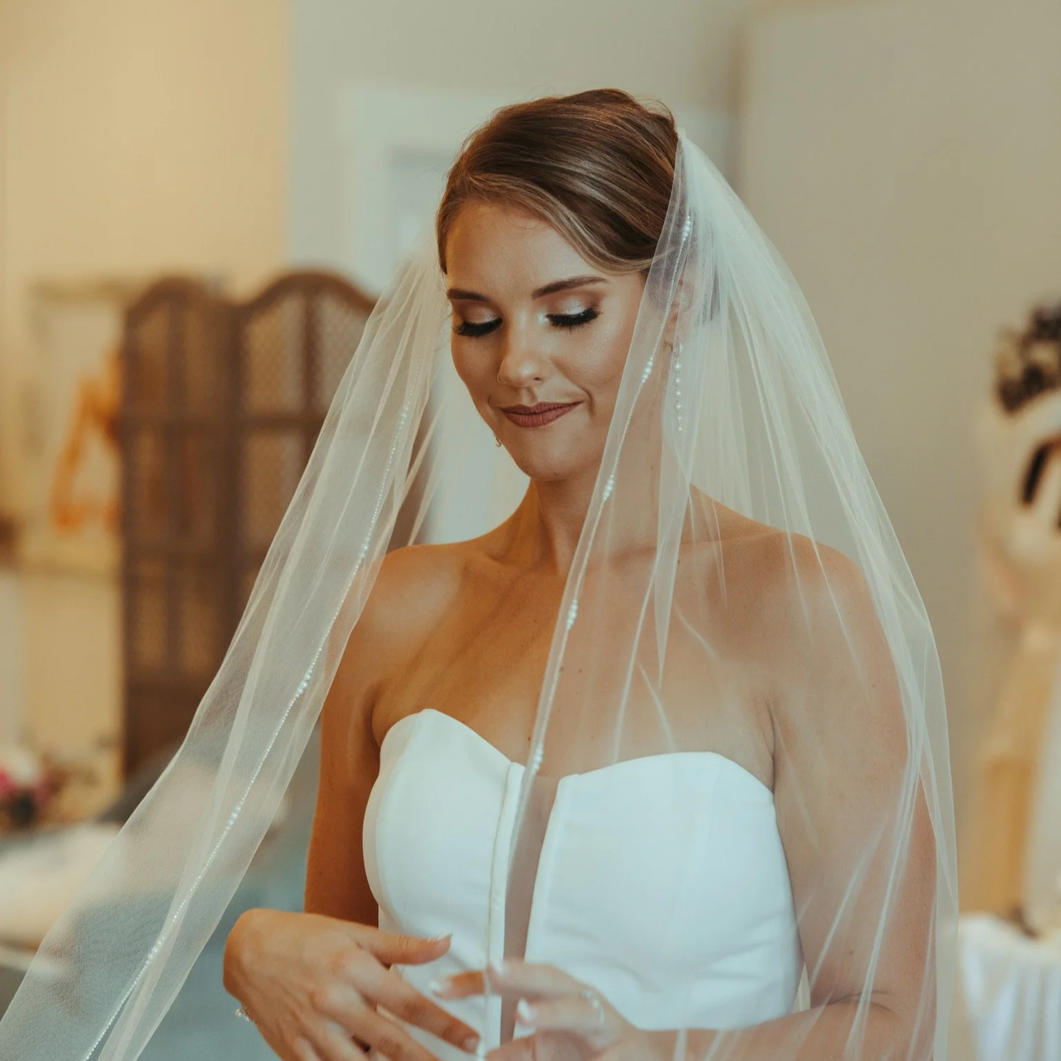 A bride wearing a white strapless wedding dress and a veil, smiling with eyes closed.