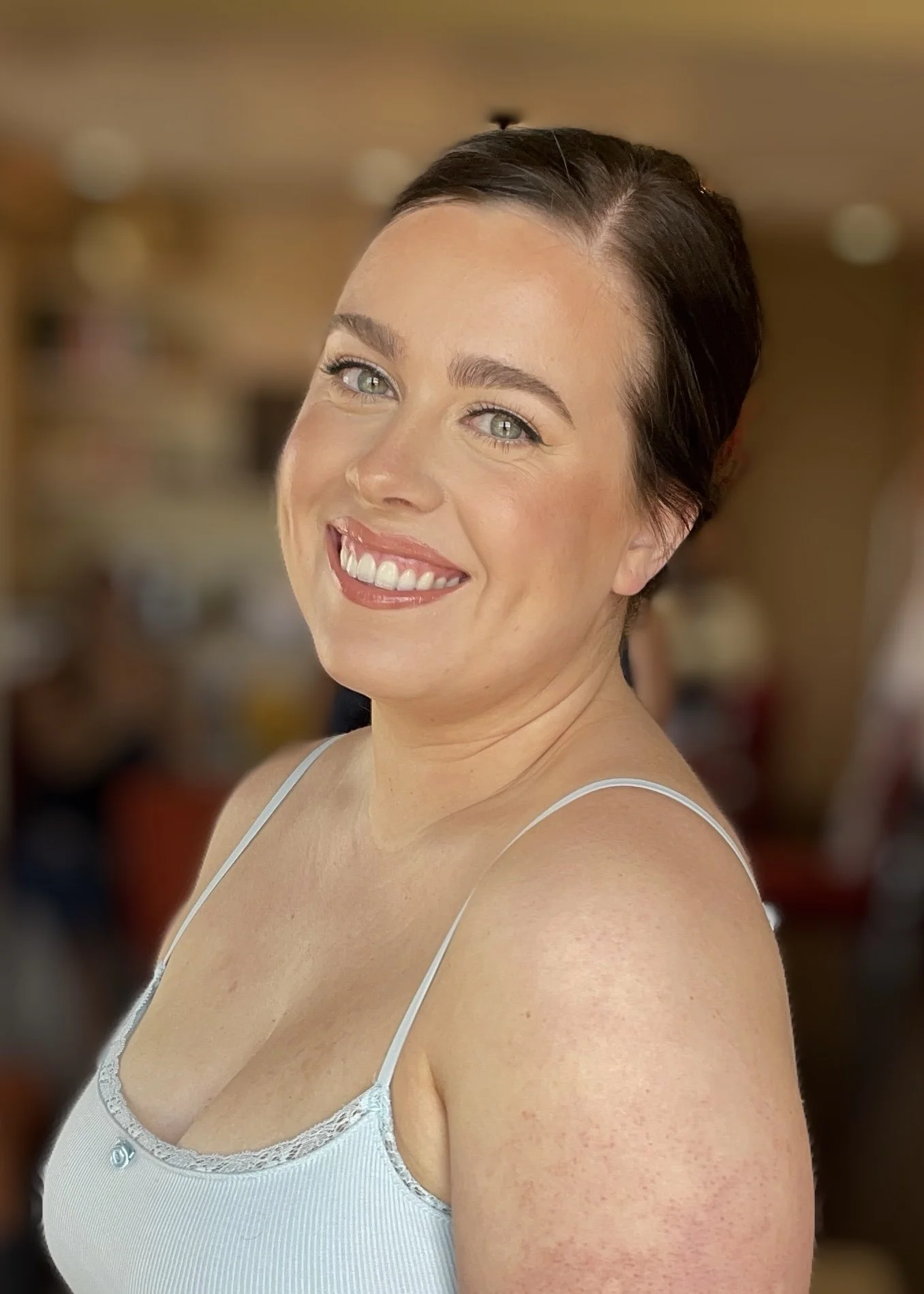 A woman with short dark hair and blue eyes smiling, wearing a white lace-trimmed camisole, with blurred background.