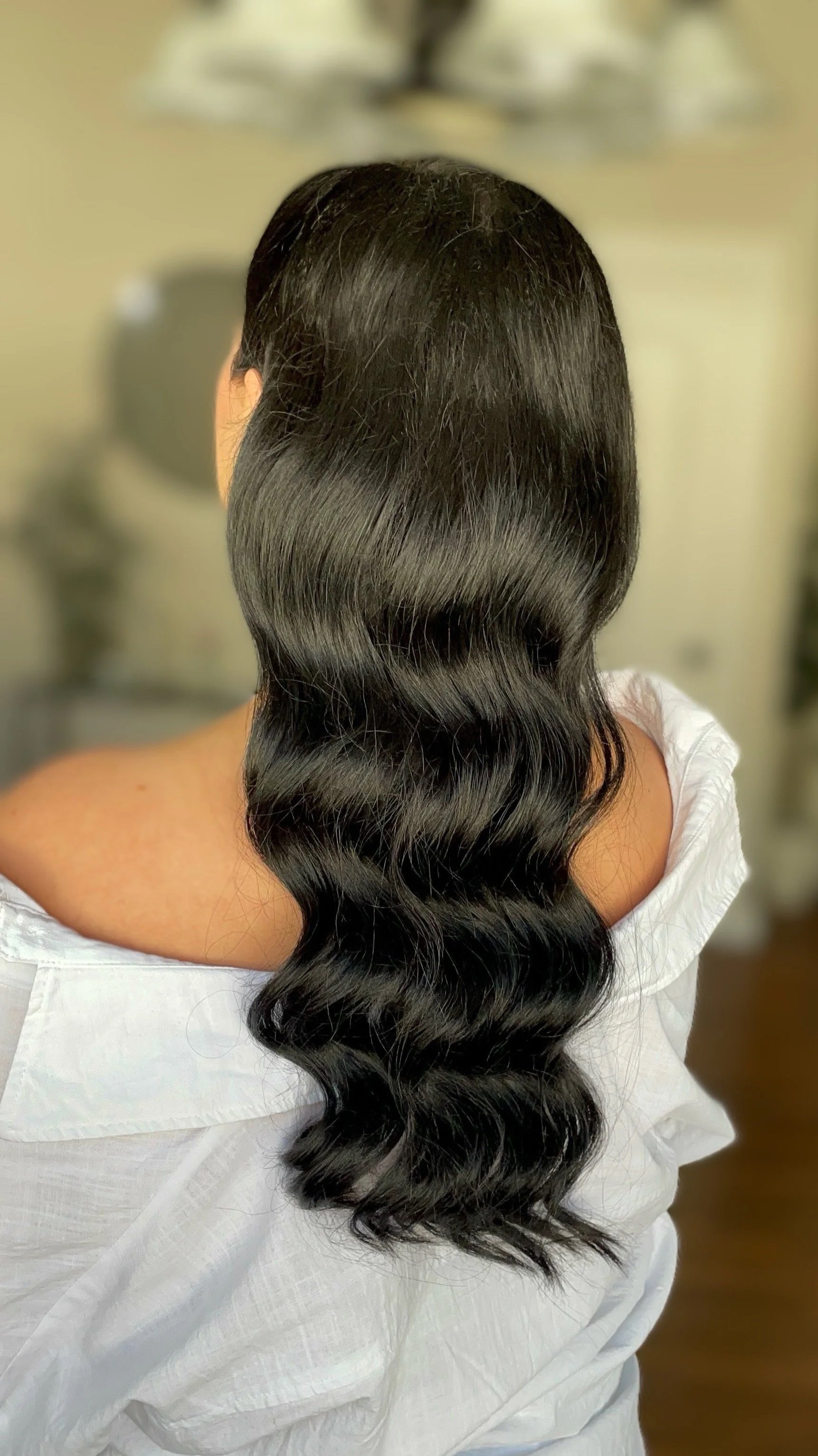 Back view of a woman with long, wavy, dark hair wearing a white garment.