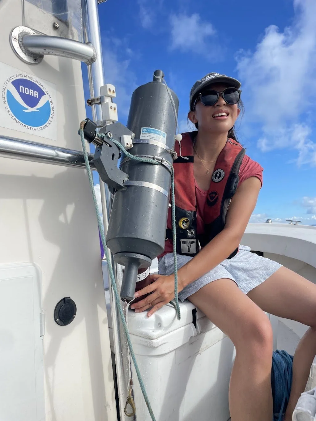 Lillian sitting on a NOAA boat using a Niskin bottle to collect samples