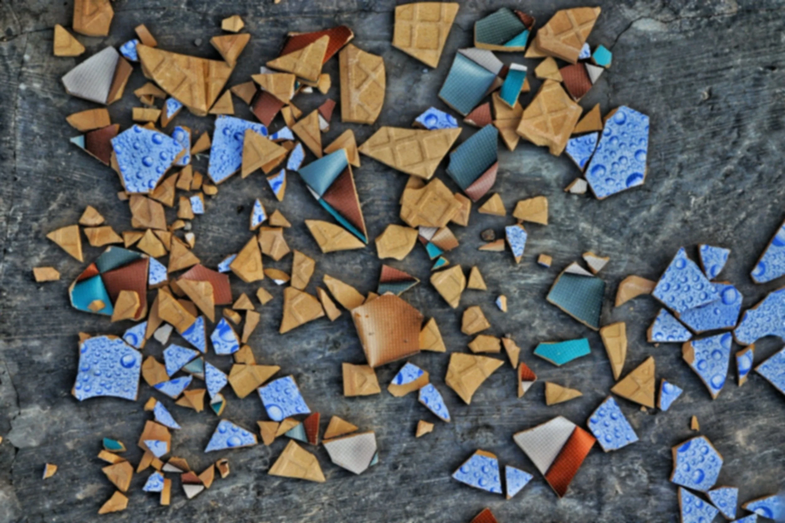 Broken ceramic tiles in various colors and patterns scattered on a weathered wooden surface.