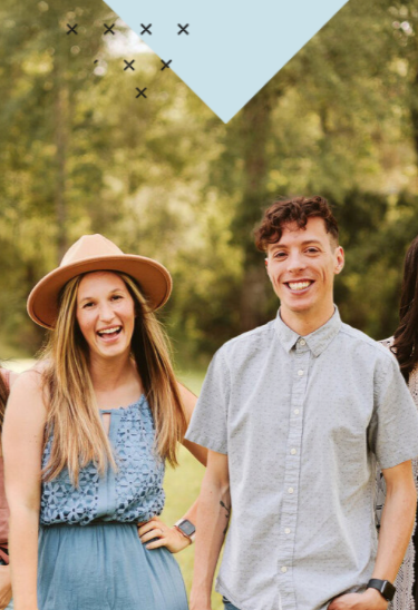 A group of young adults outdoors, smiling and enjoying a sunny day, with lush green trees in the background.