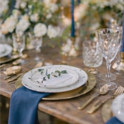 Elegant table setting with a white plate, blue napkin, and glassware, surrounded by floral arrangements.
