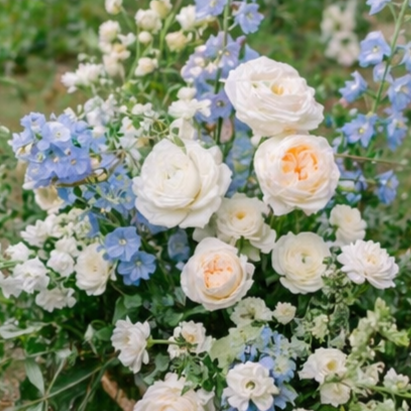 A bouquet of white and light peach roses with blue and white smaller flowers and green foliage.