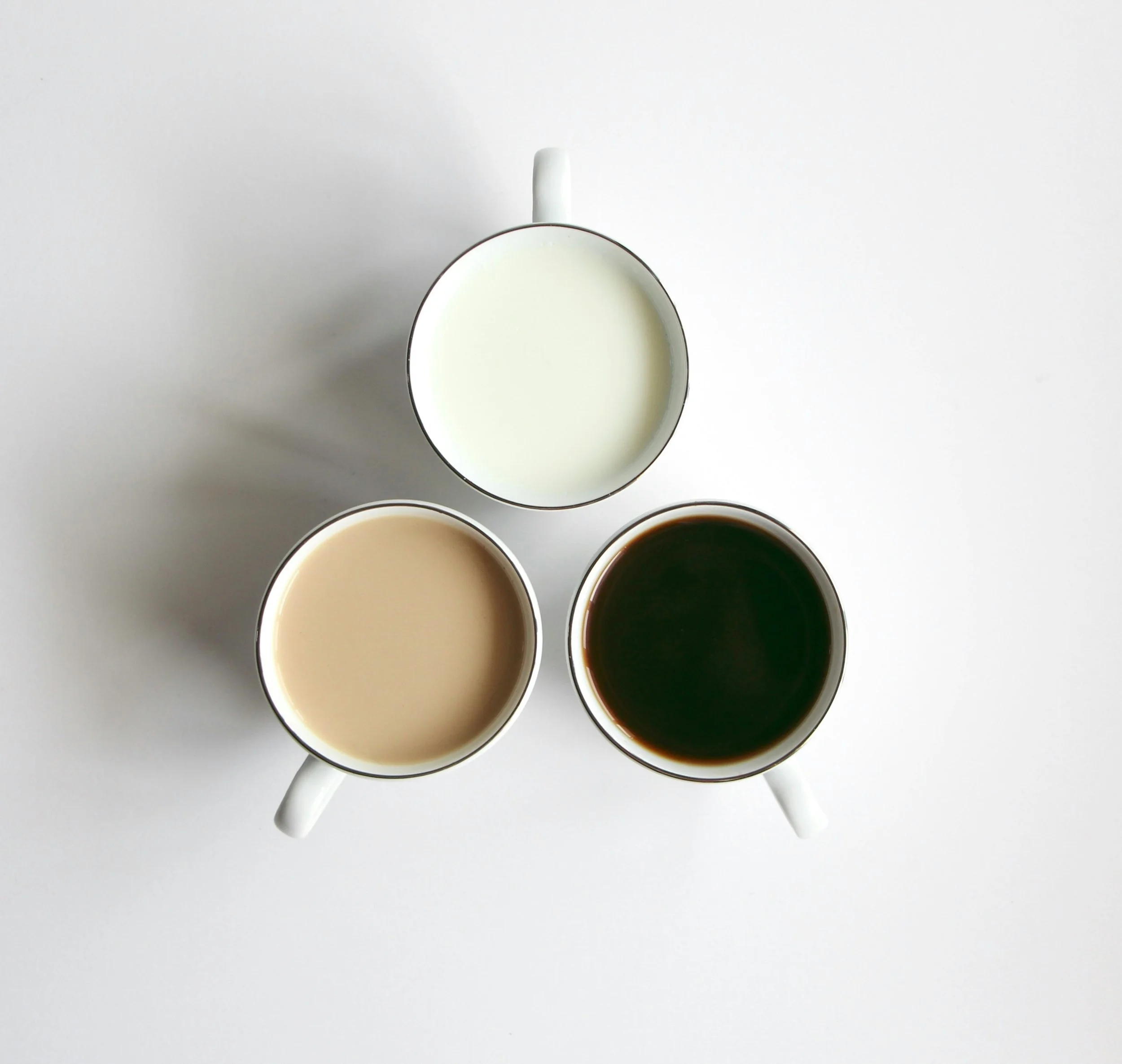 Top-down view of four white ceramic coffee cups filled with different dark liquids, arranged on a white surface.