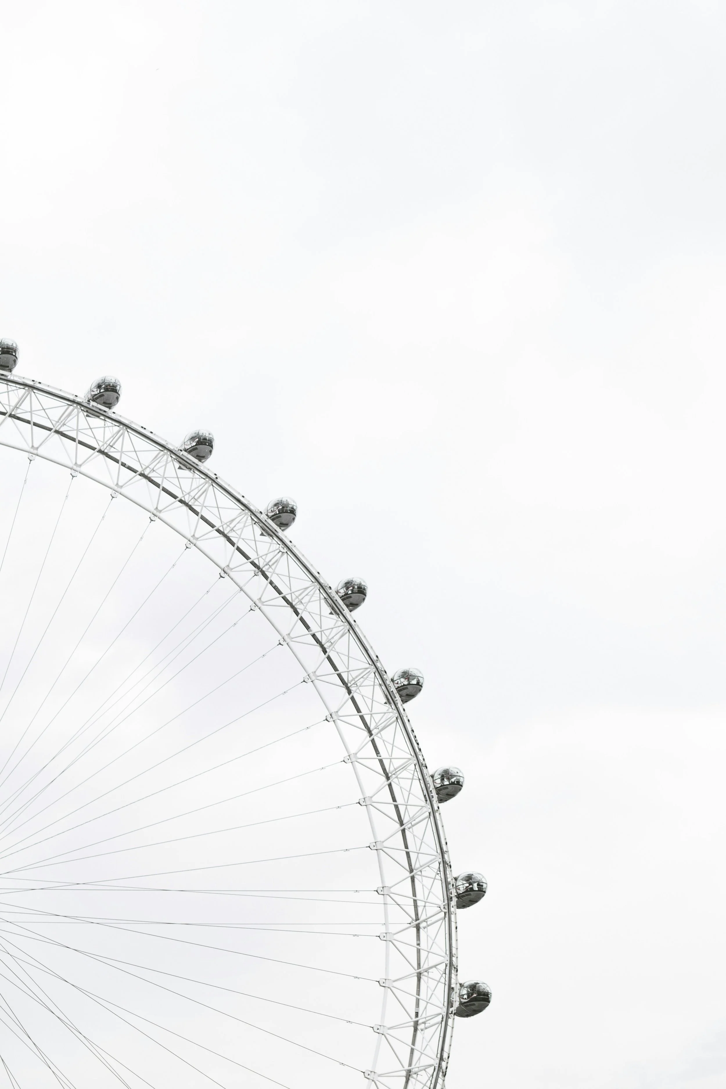 Part of the London Eye Ferris wheel with glass capsules against a grey sky.