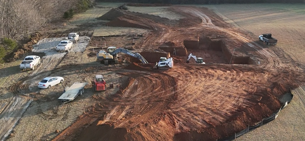 Construction site with multiple vehicles including trucks and cars, and large excavated areas in a rural field.