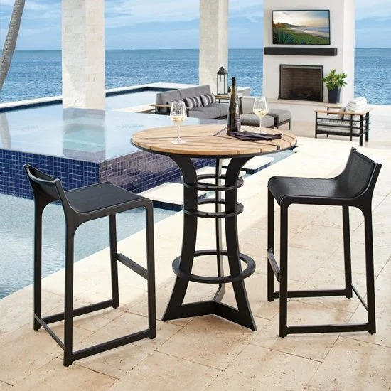 Outdoor patio with a high table and two chairs overlooking a pool and ocean, with a TV and fireplace in the background.