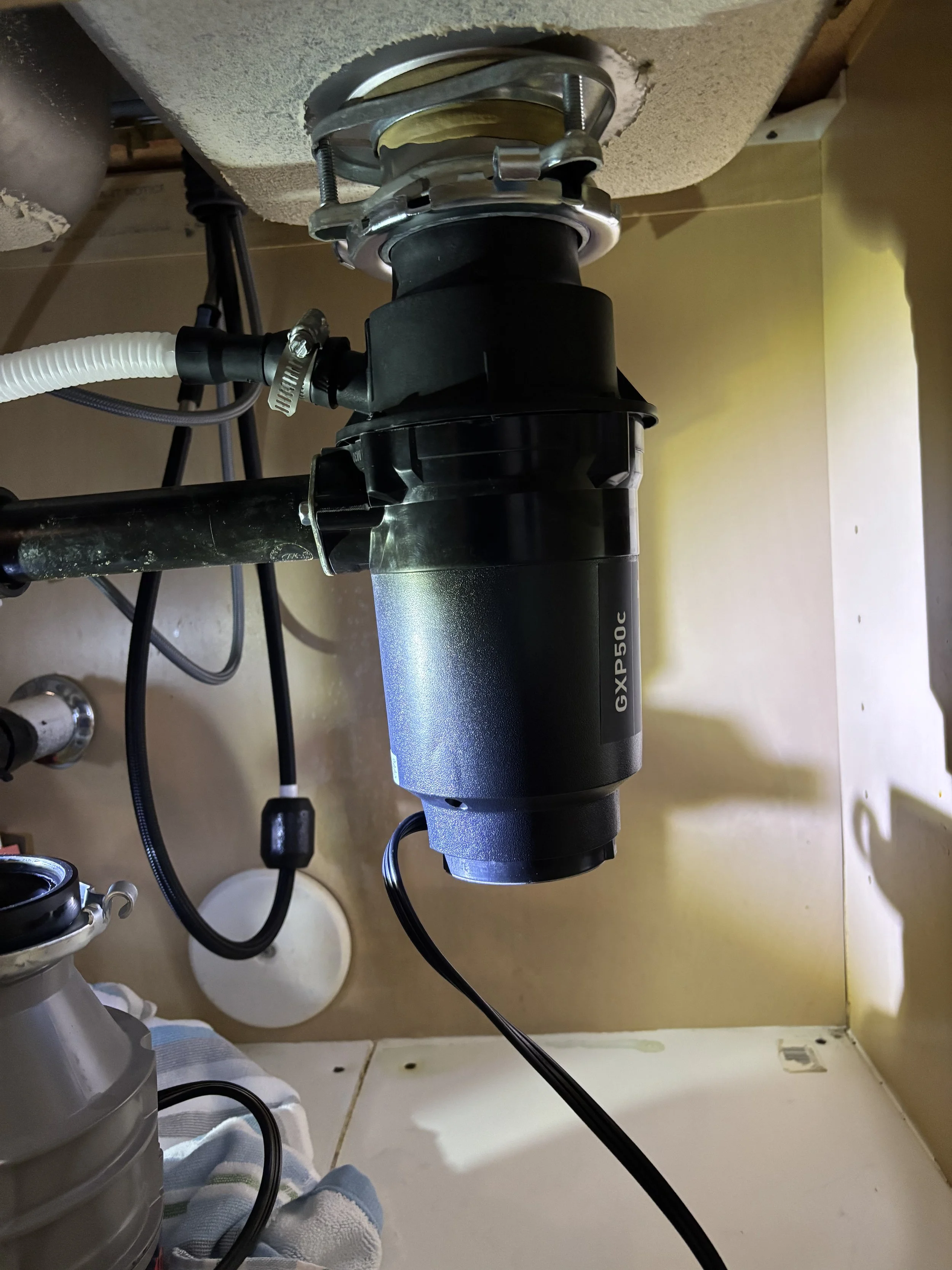 View of plumbing under a sink showing a black garbage disposal unit with pipes and hoses connected.