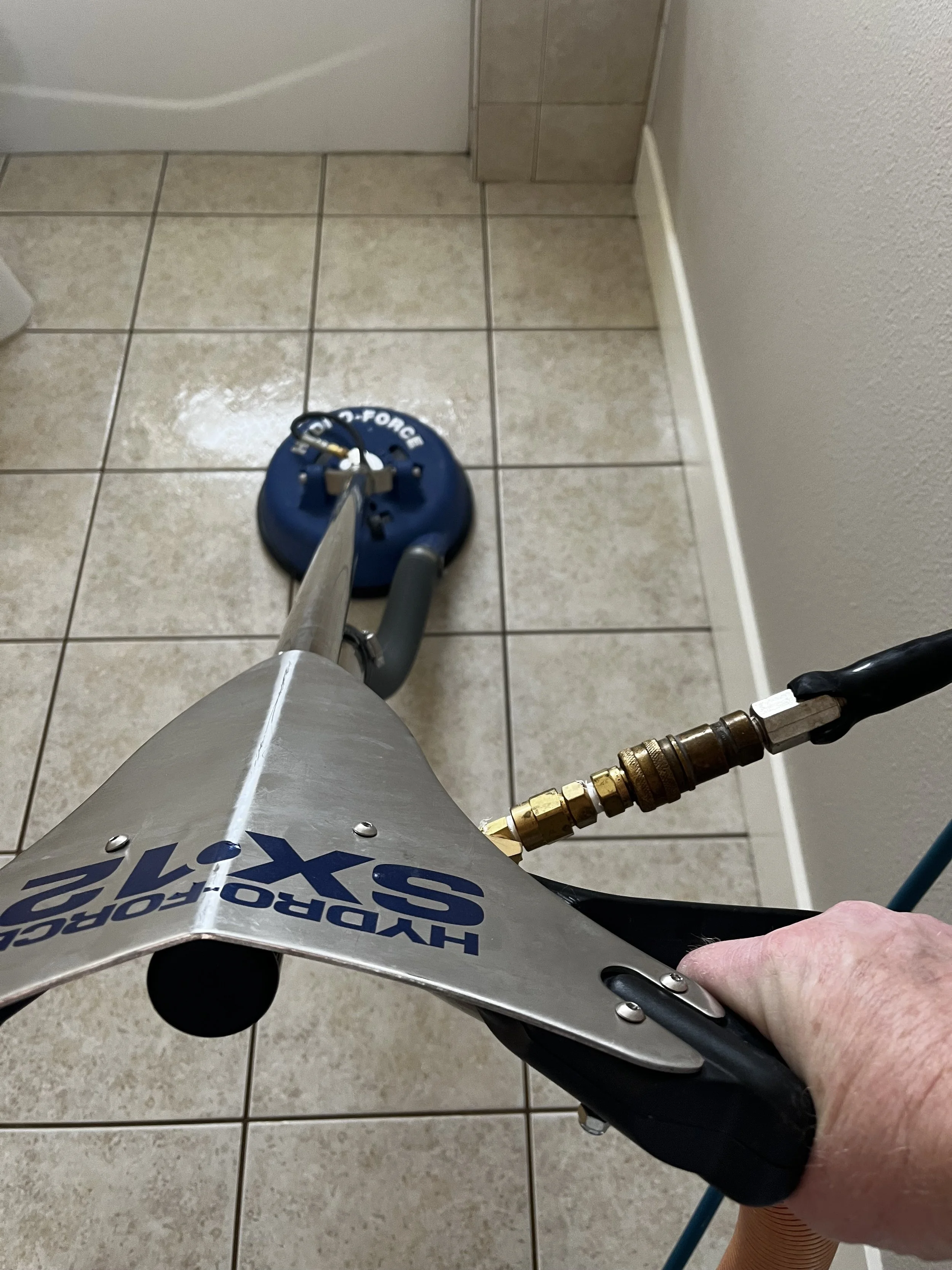 A person holding a pressure sprayer labeled 'HYDROGEN-2-FOAM' in a room with tiled floor and wall, using the sprayer nozzle for cleaning or disinfecting.