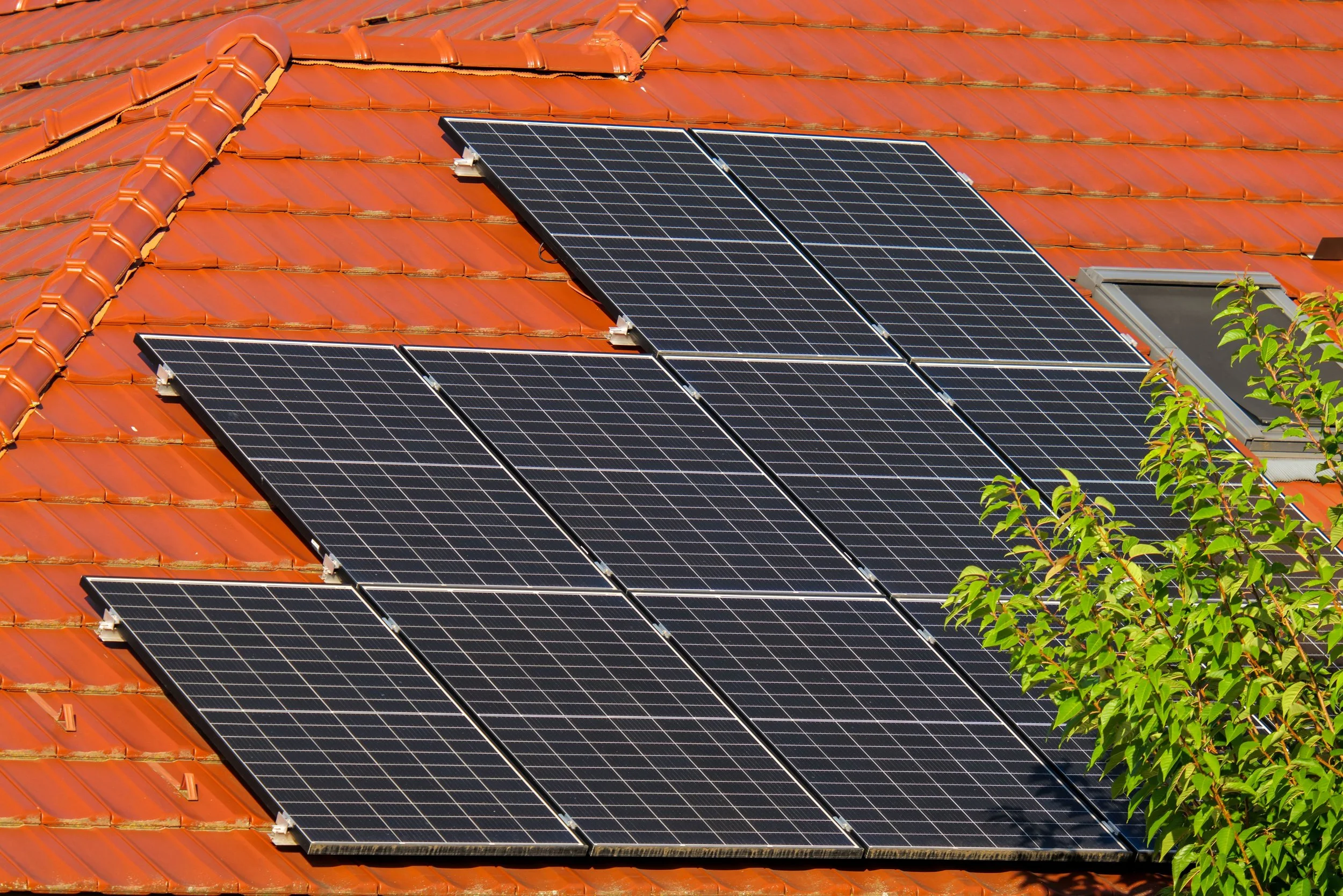 Solar panels installed on a red tiled roof with some green foliage visible in the lower right corner.