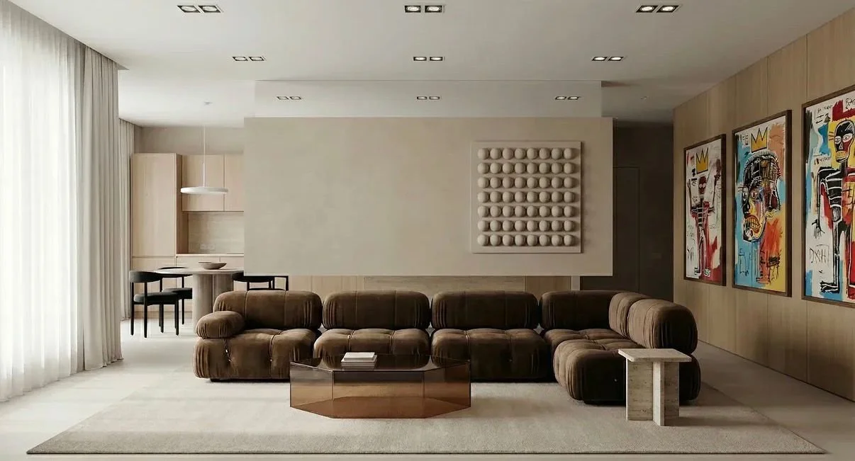 Sala de estar moderna con sillones de tela marrón, mesa de centro de cristal, paredes de madera, arte abstracto en las paredes, cortinas blancas y espacio de comedor en el fondo.