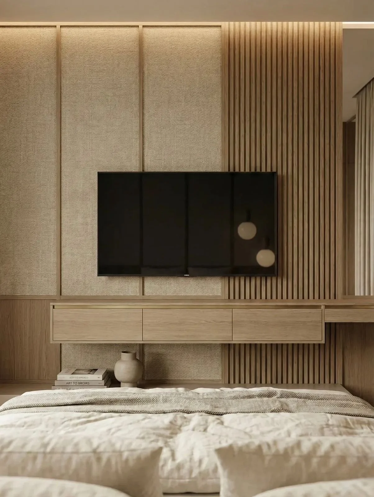 Una pared de madera decorativa con un televisor de pantalla plana en el centro, un mueble debajo, y una cama en primer plano, con algunos libros y una vasija decorativa en la mesa de noche.
