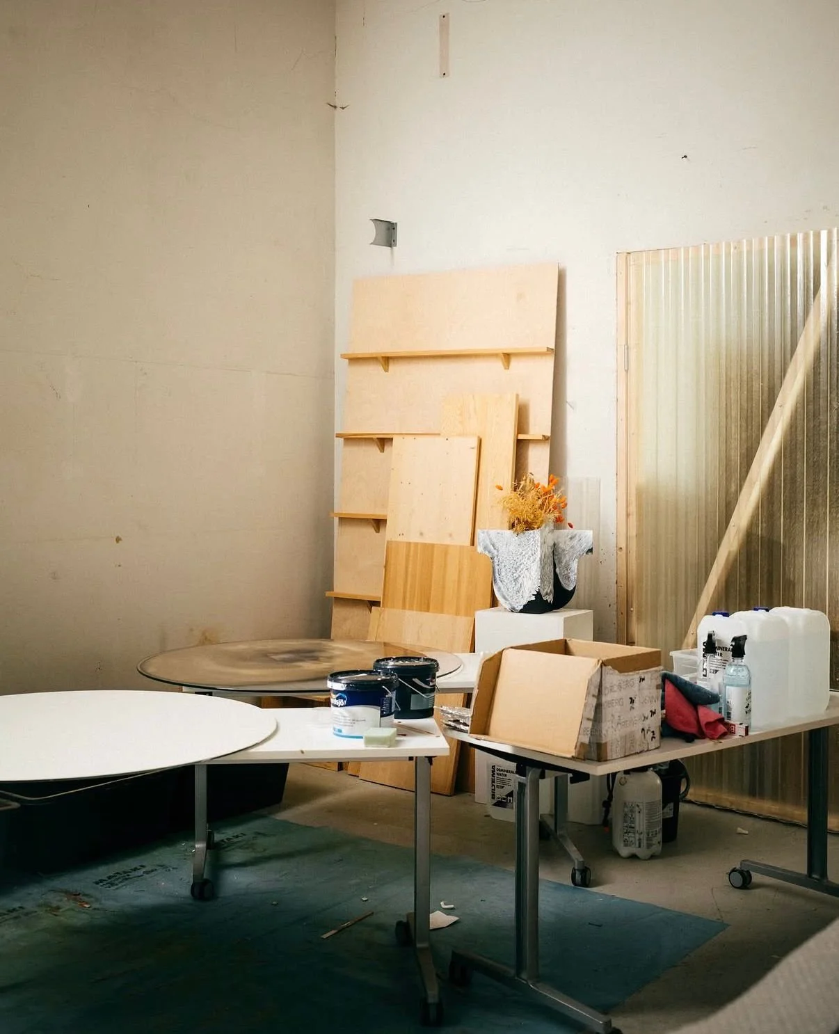 Espacio de trabajo con mesas, pintura en tarros, y madera almacenada, en un ambiente de construcción o taller.