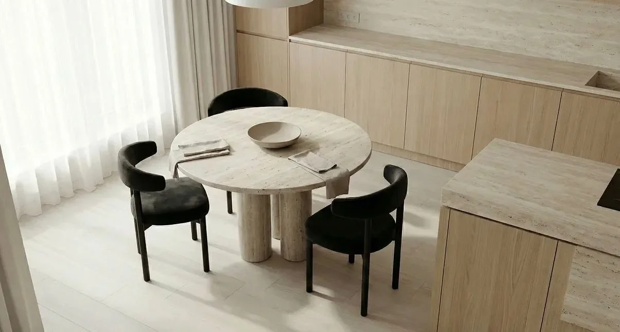 Mesa de comedor redonda con cuatro sillas negras, cerámica clara, con mantel, servilletas y plato en un ambiente minimalista.