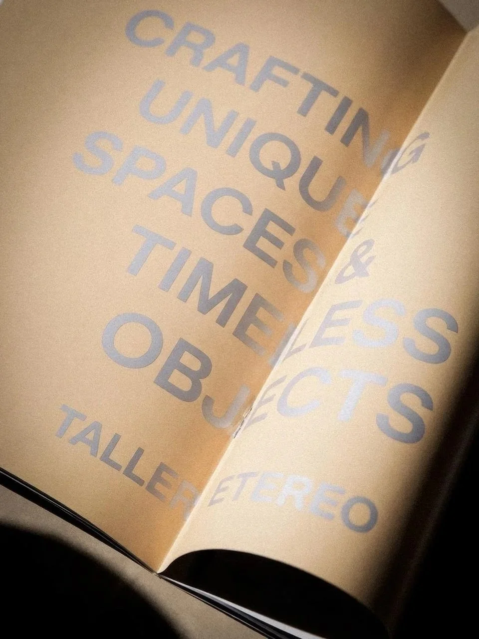 Página de cuaderno con texto en letra grande que dice 'Crafting Unique Spaces & Timeless Objects' en color gris claro sobre fondo beige.