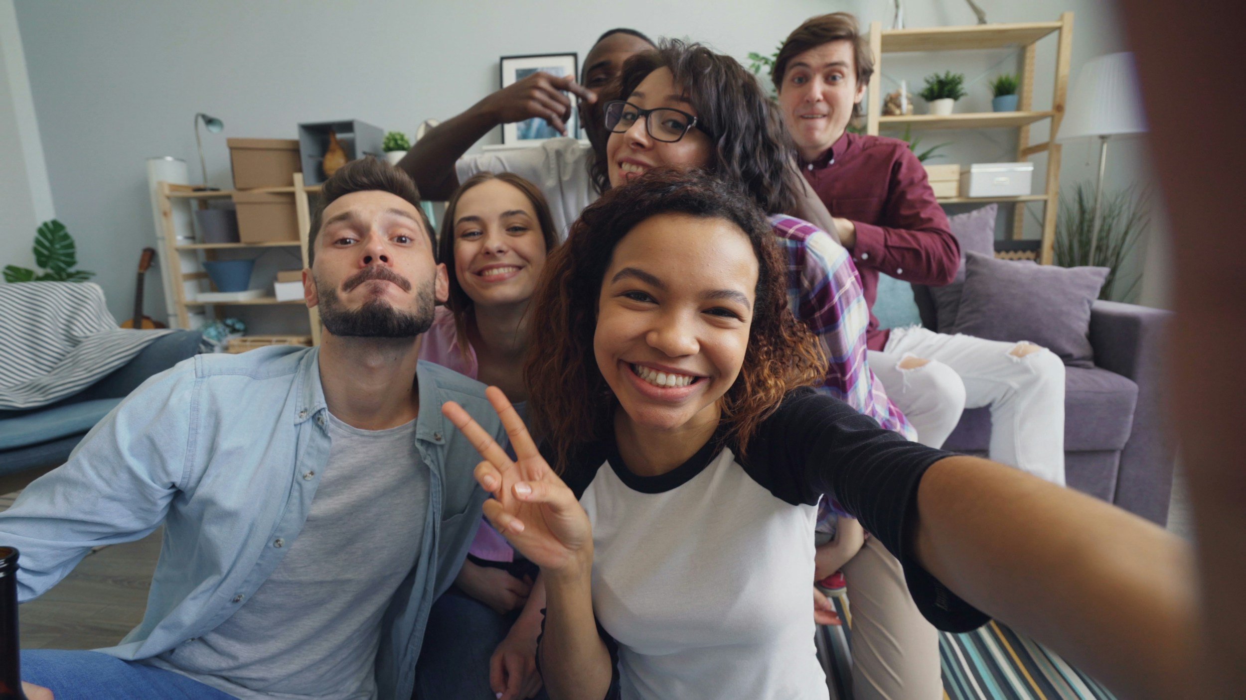 Group of six young adults taking a selfie together in a living room.