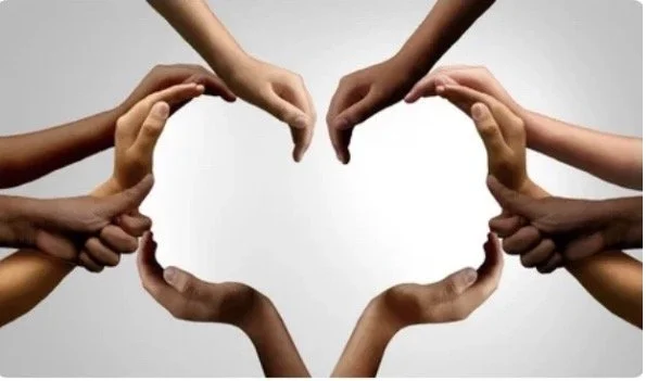Multiple hands of various skin tones forming a heart shape against a plain background.