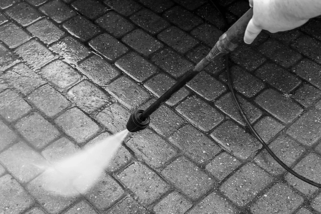 A person pressure washing a brick sidewalk.